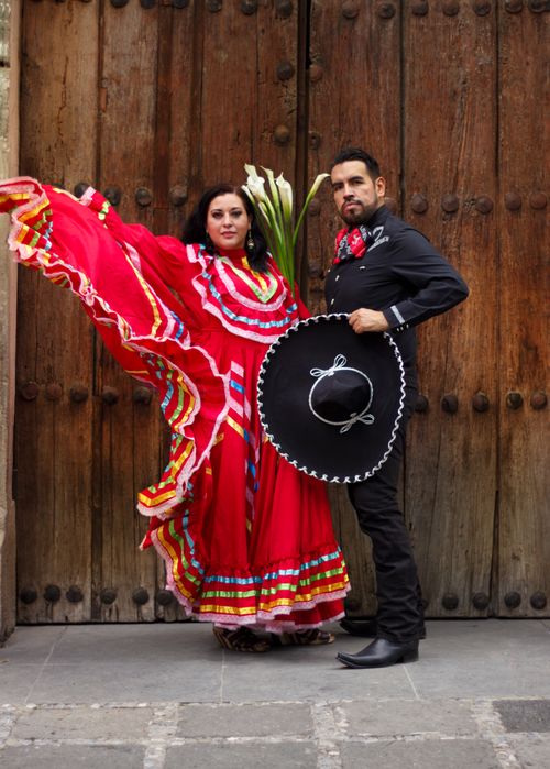 Free Mexican couple in traditional attire dancing gracefully against a historic wooden door. Stock Photo