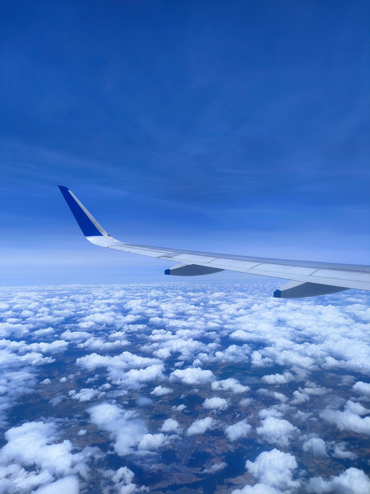 View from an airplane wing flying above clouds and land