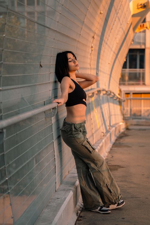 Free Stylish woman in cargo pants and black top posing on an urban bridge at sunset. Stock Photo
