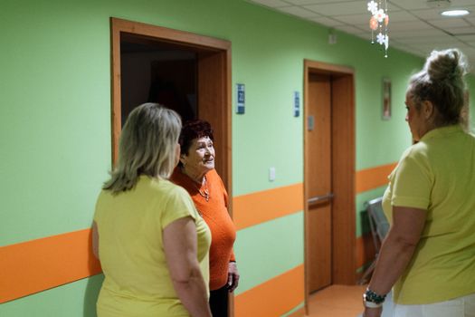Senior woman engages in conversation with caregivers in a facility corridor.