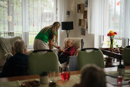 Caregiver assisting elderly women with tea in a cozy nursing home setting