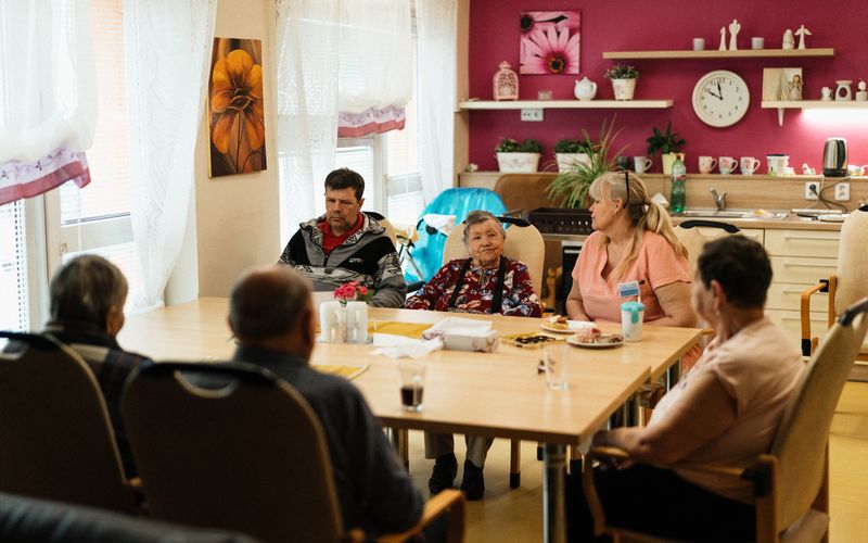 Caregiver assisting seniors at dining table — help with daily routines and meals