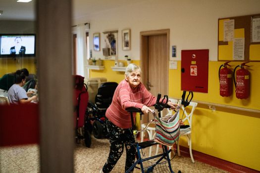 Senior woman using a walking frame in a cozy nursing home interior in Karviná, Czech Republic.