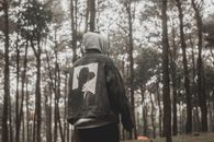 穆迪森林场景中，一个身穿牛仔夹克的人站在树木环绕之处，捕捉冒险的感觉