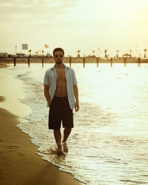 Man in Sunglasses and Shirt Walking on Sea Shore at Sunset