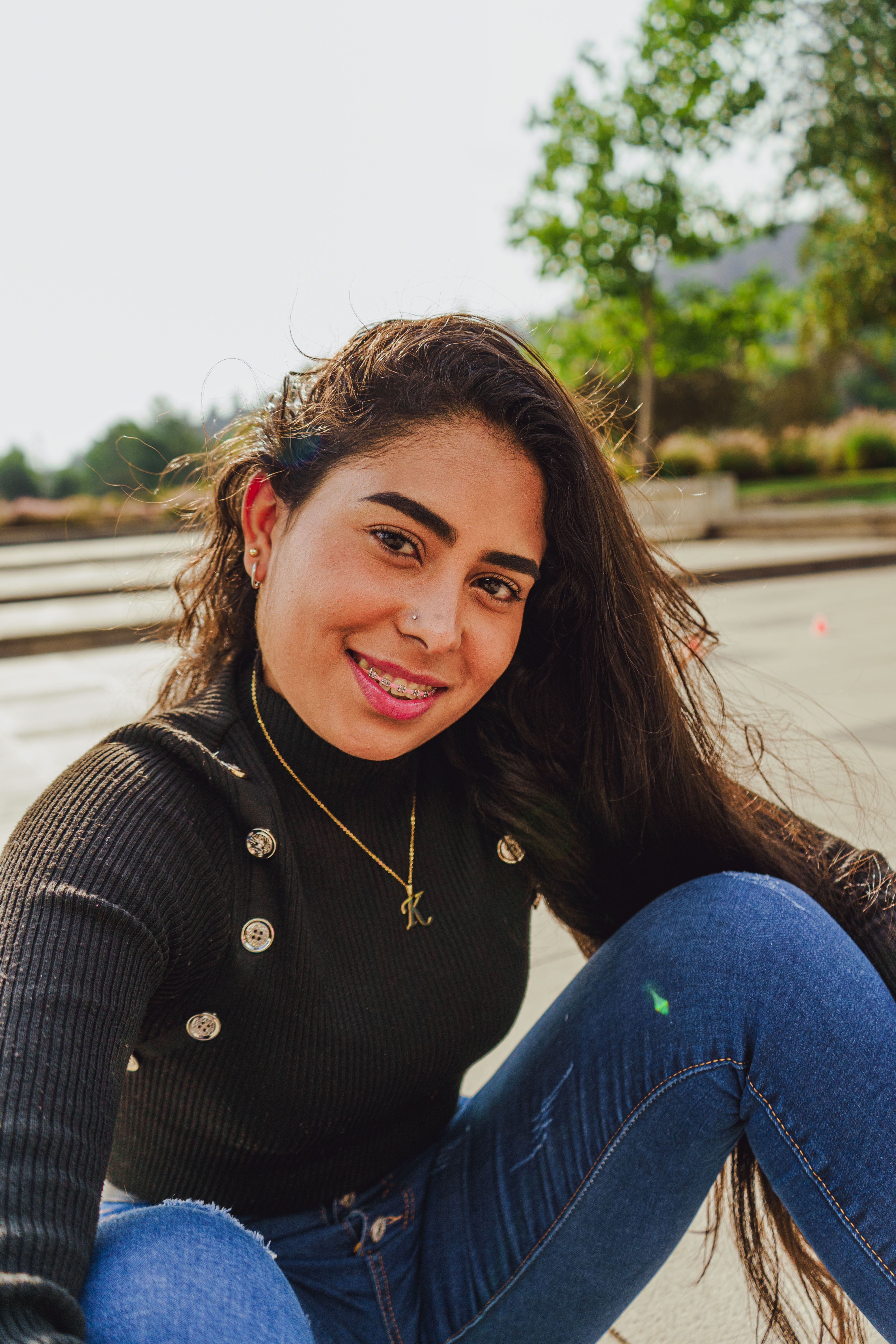 Cheerful young woman with long hair and a necklace smiling outdoors.