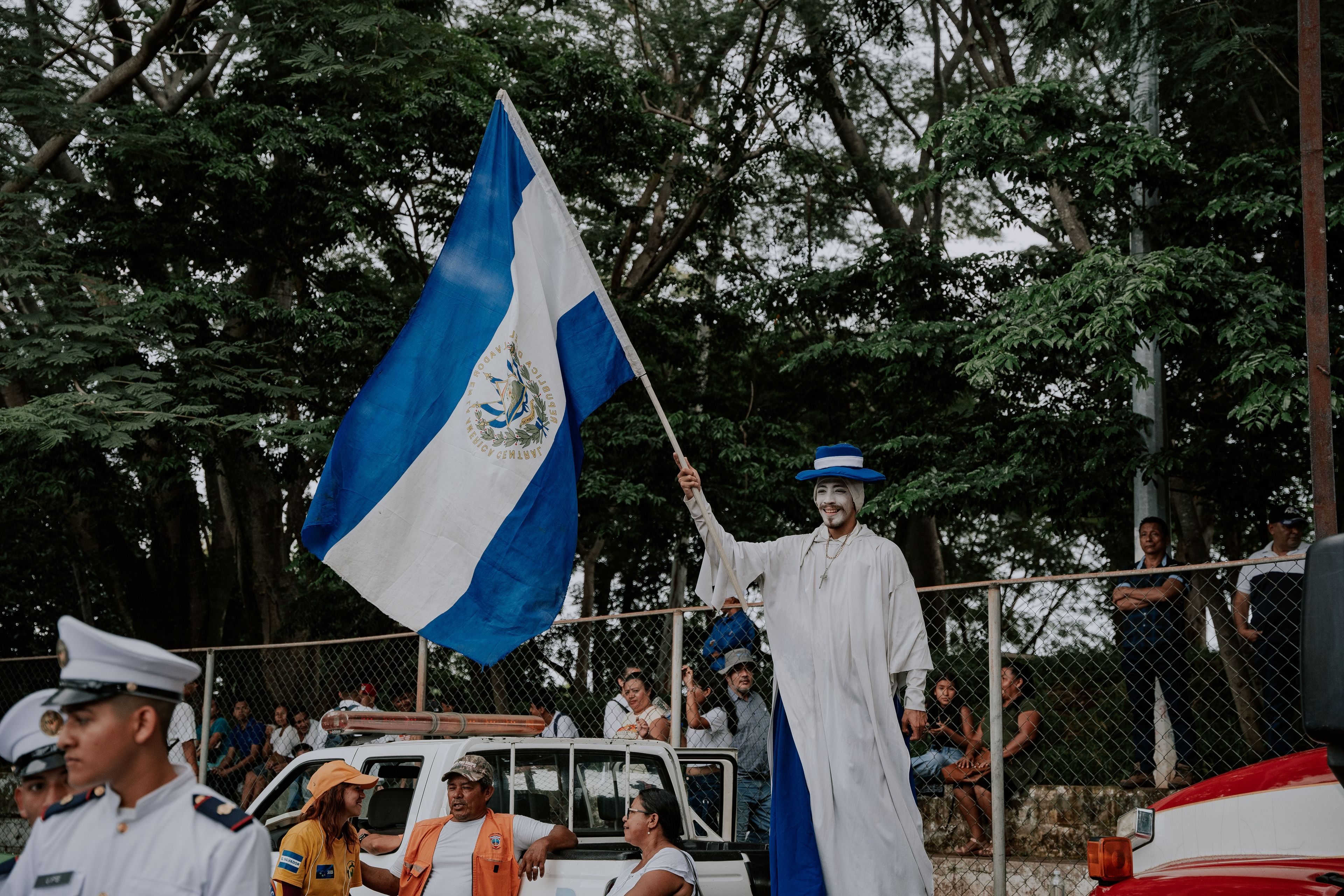 A festive parade participant proudly waves the El Salvador flag outdoors.