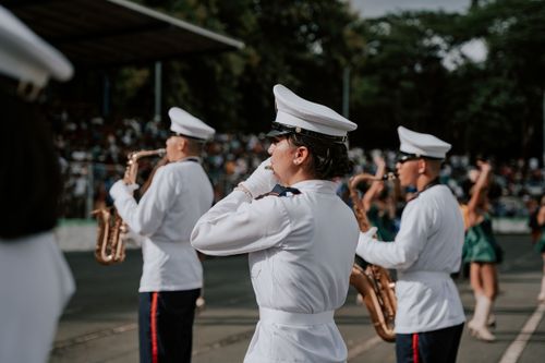 Free Military band playing in a parade with musicians in white uniforms and saxophones outdoors. Stock Photo