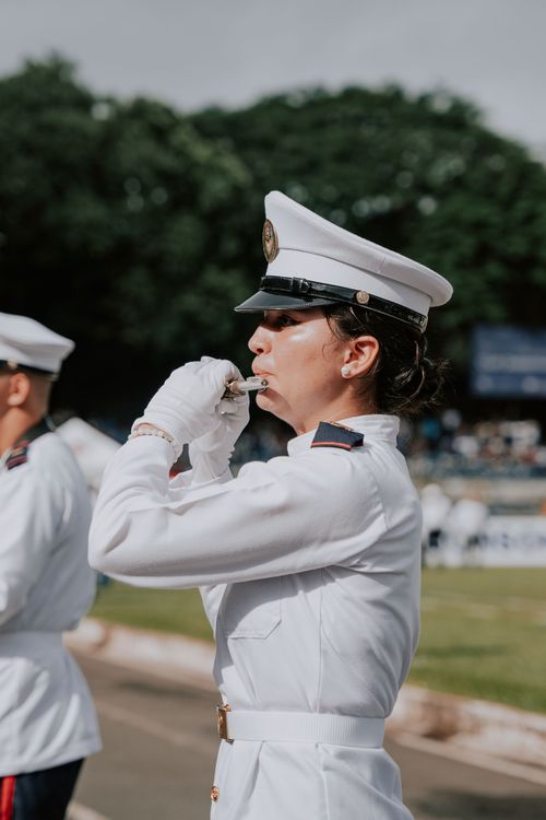 Free A woman soldier in a white uniform playing a flute during a parade outdoors in El Salvador. Stock Photo