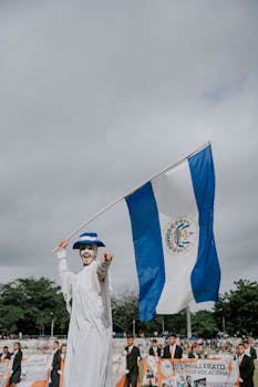 Festive performer in El Salvador waving national flag in outdoor celebration.