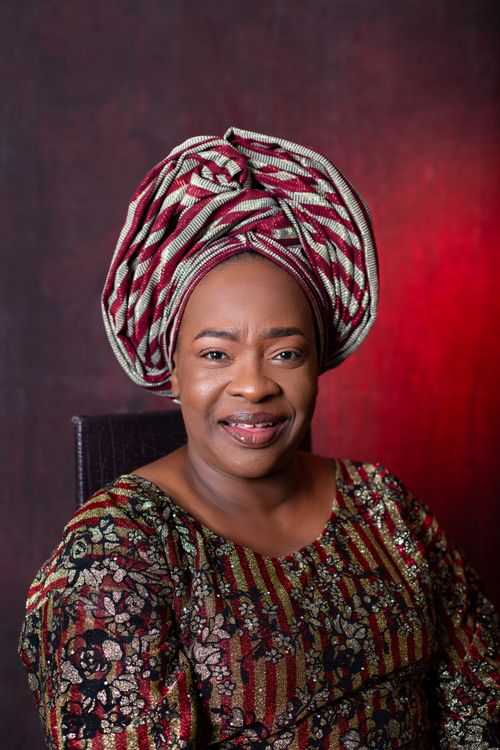 Free Smiling woman in traditional attire with a vibrant headdress against a red backdrop, studio setting. Stock Photo