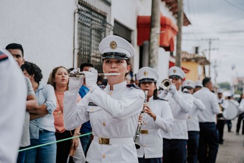 Free A marching band in white military uniforms parades down a city street, playing instruments. Stock Photo