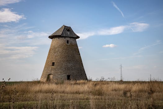 A medieval stone windmill stands in a grassy field in rural Serbia under a blue sky.