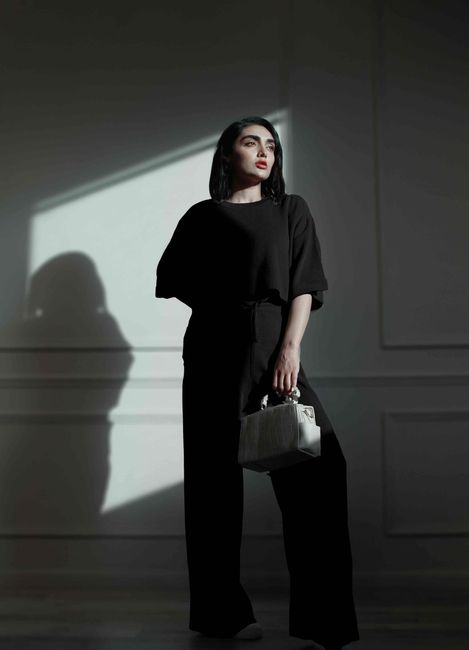 Elegant portrait of a woman in black attire holding a handbag under striking lighting. - Handbag Styles That Complement Each Body Type