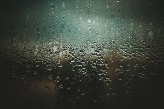 Close-up of raindrops on a glass window with a dark and moody ambiance.