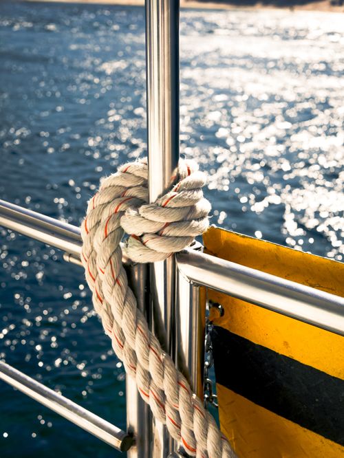 Free Close-up of rope tied on a ship railing with ocean backdrop, glistening water. Stock Photo