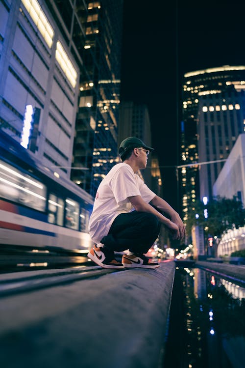 Man Crouching against Illuminated Skyscrapers at Night