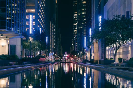 A stunning night view of a city street with reflective water and illuminated buildings.