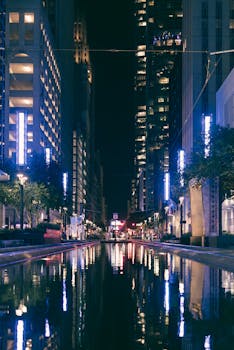 Illuminated cityscape at night with skyscrapers reflecting in a canal.