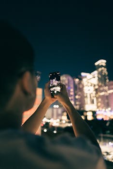 Person photographing city skyline at night using a smartphone.