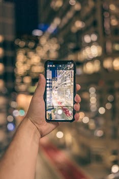 A hand holding a smartphone capturing an illuminated city at night, showcasing urban photography.