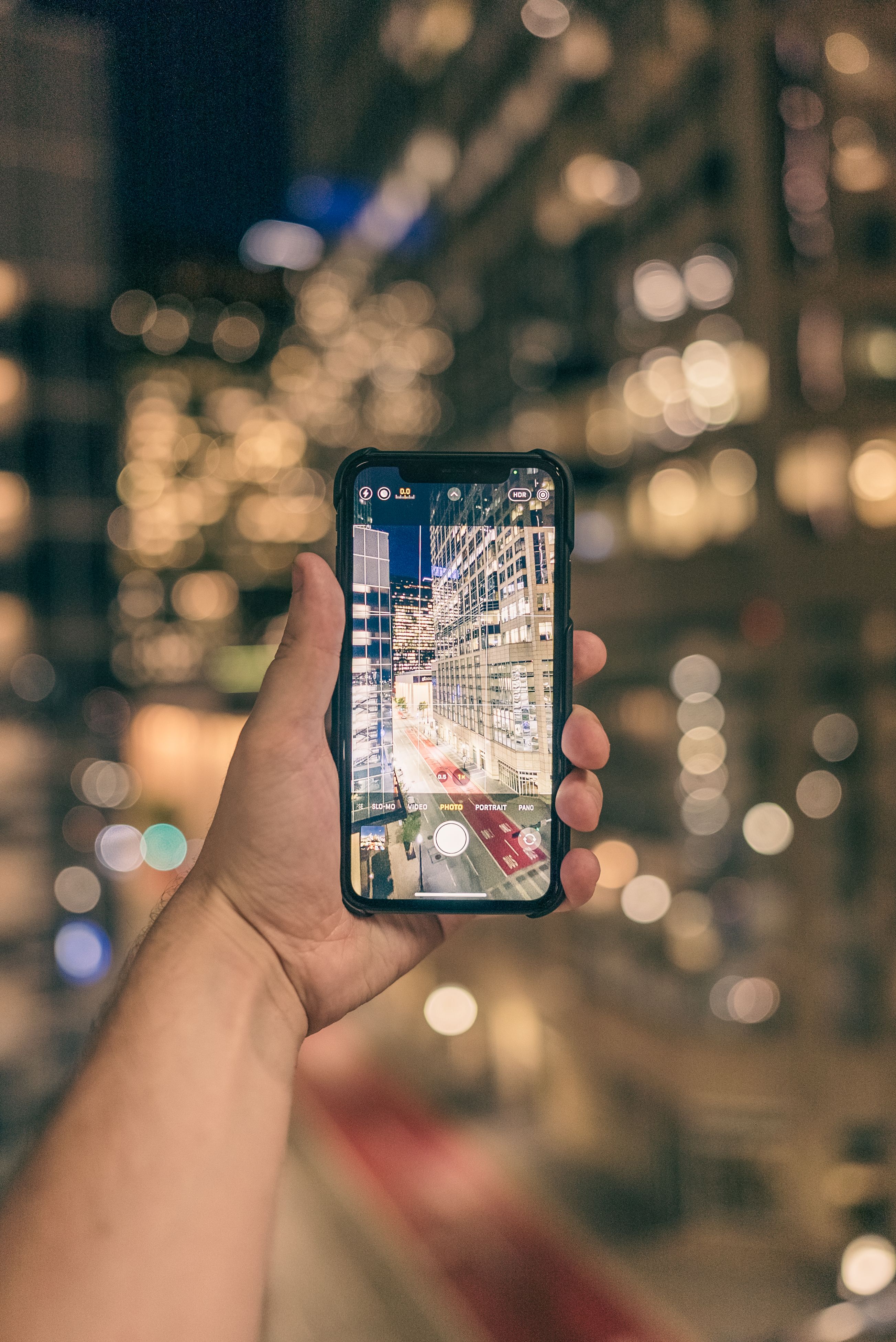 Free A hand holding a smartphone capturing an illuminated city at night, showcasing urban photography. Stock Photo