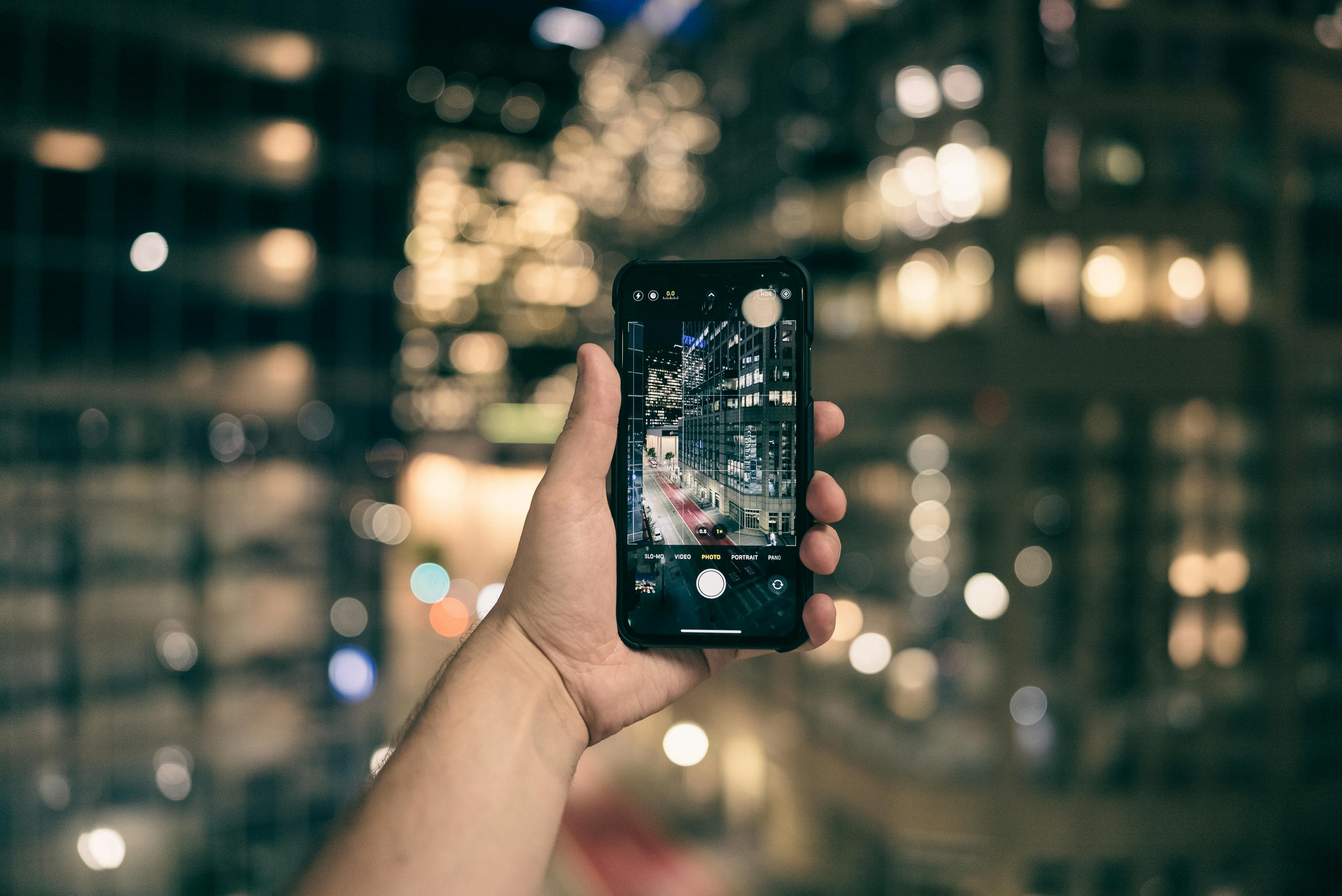 Close-up of hand holding a smartphone capturing a vibrant cityscape at night.