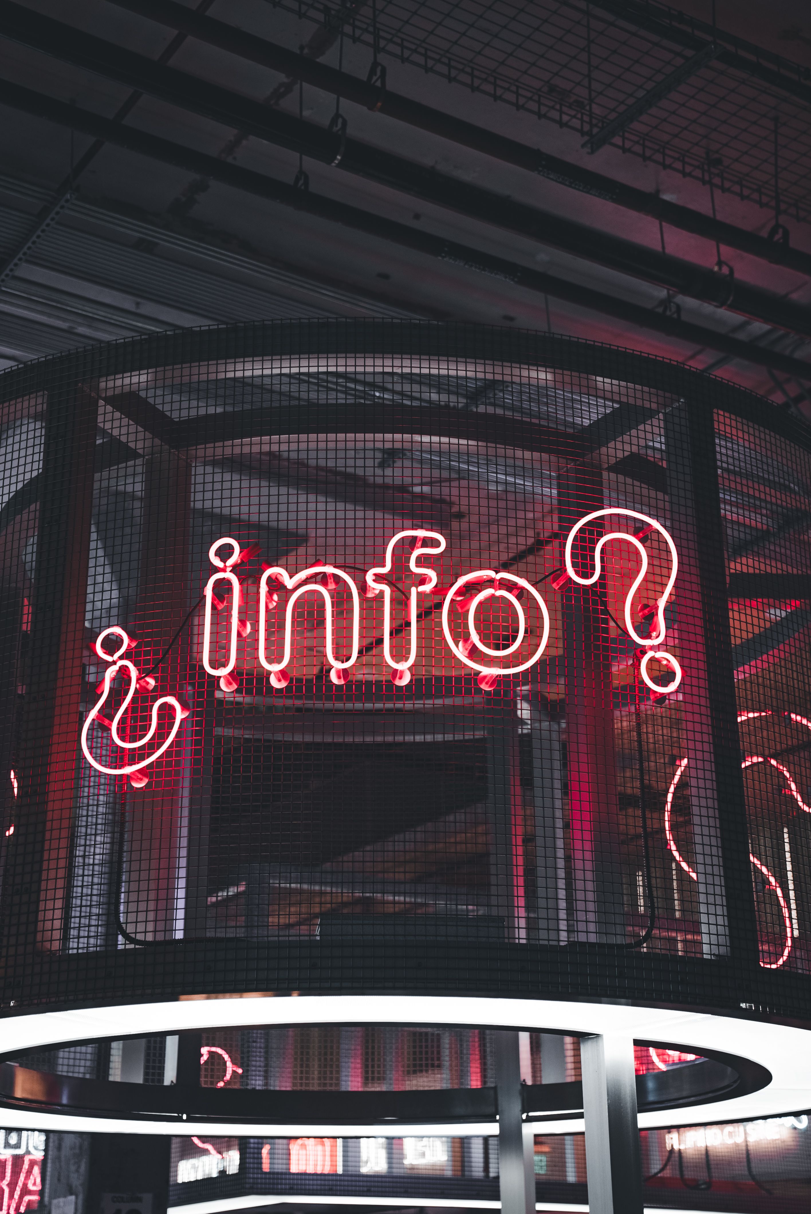 Close-up of a glowing neon info sign with urban background.