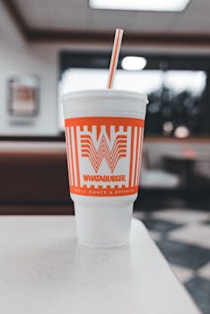 Close-up of a Whataburger cup with a straw positioned on a table in a fast-food restaurant setting.