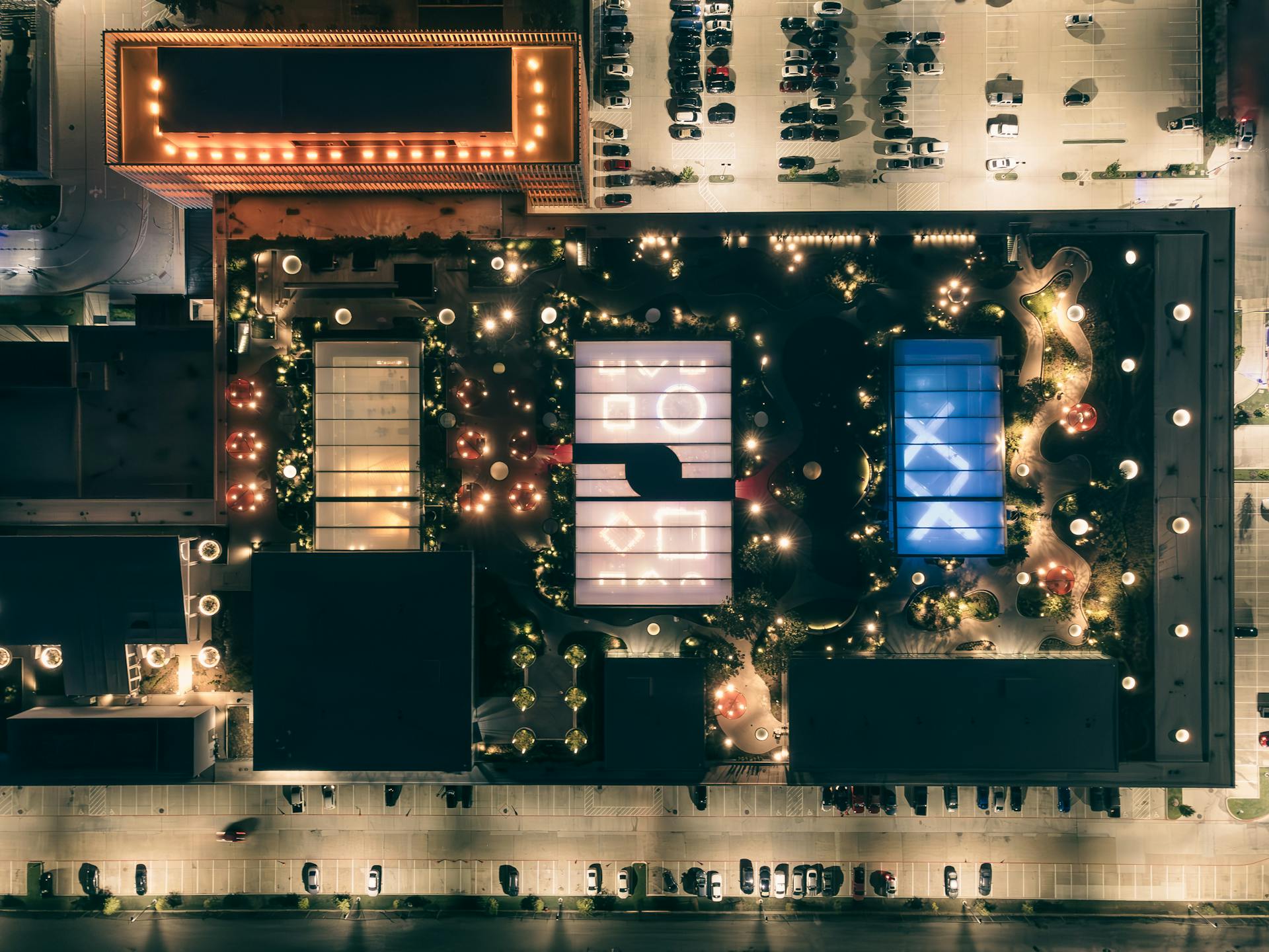 Stunning aerial shot of a beautifully lit urban rooftop garden at night with geometric patterns and glowing lights.