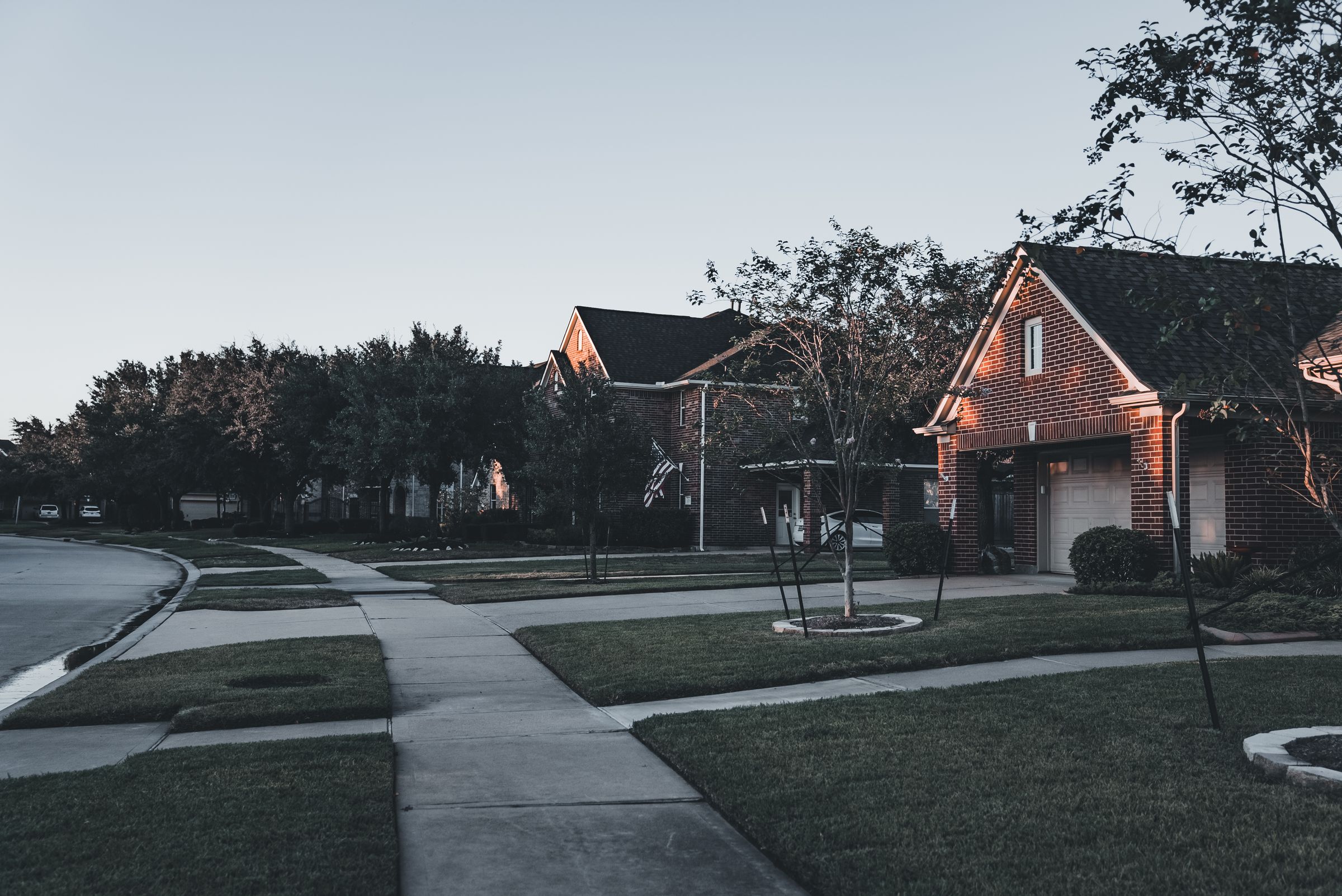 Contemporary brick house at dusk with warm interior light spilling into the garden