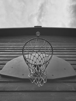 Basketball hoop with a net on a wooden backboard under a cloudy sky.
