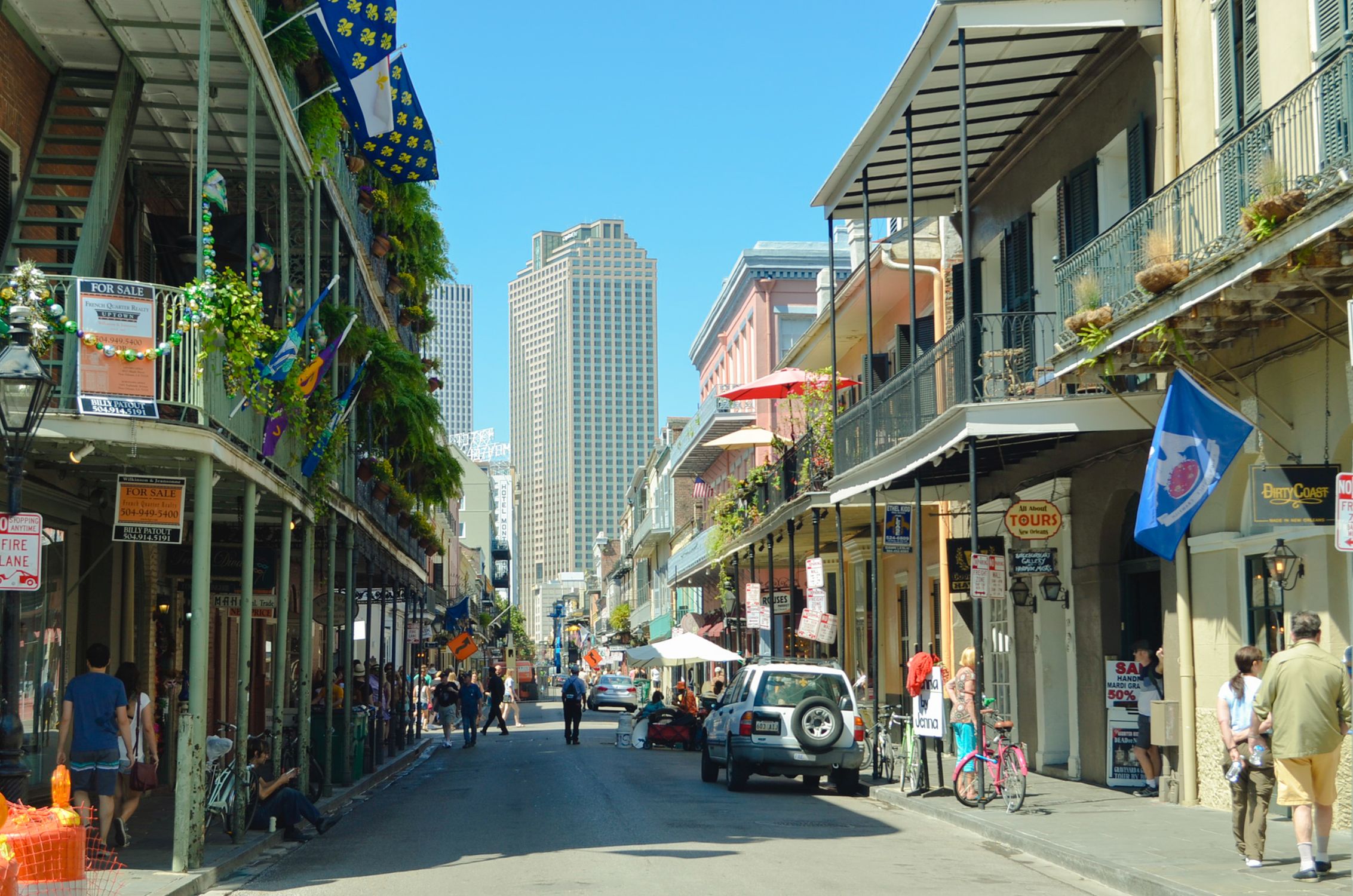 Explore a lively New Orleans street bustling with pedestrians, cars, and iconic architecture under a clear summer sky.