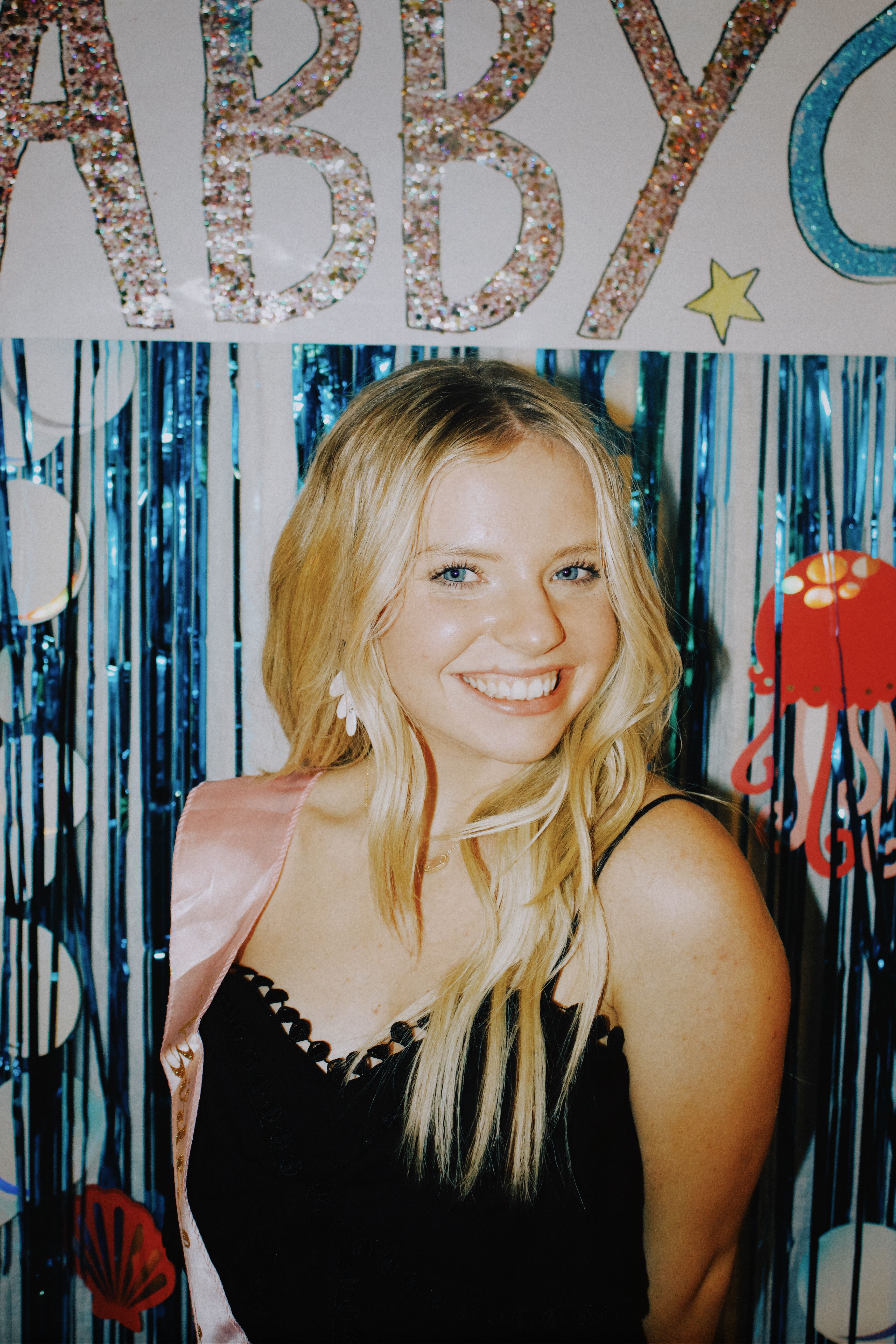 Smiling woman in a black dress at a festive celebration, exuding glamour and joy.