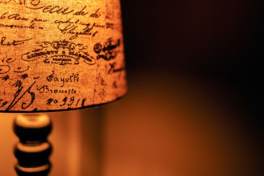 Close-up of a vintage lamp with a scripted fabric shade, casting warm light indoors.