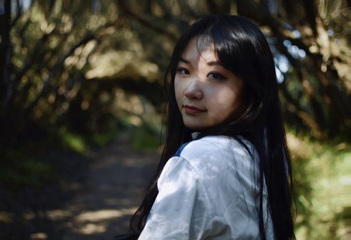 Young woman with long hair walking through a sunlit forest path, looking over her shoulder.