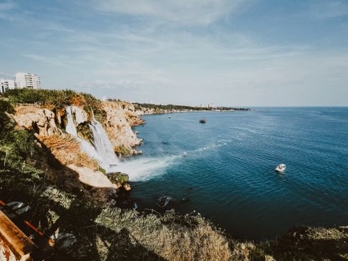 Free Stunning view of a waterfall cascading over a cliff into the ocean under a bright blue sky. Stock Photo