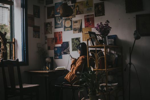 Asian woman relaxing in a vintage living room, using a cellphone surrounded by retro decor.