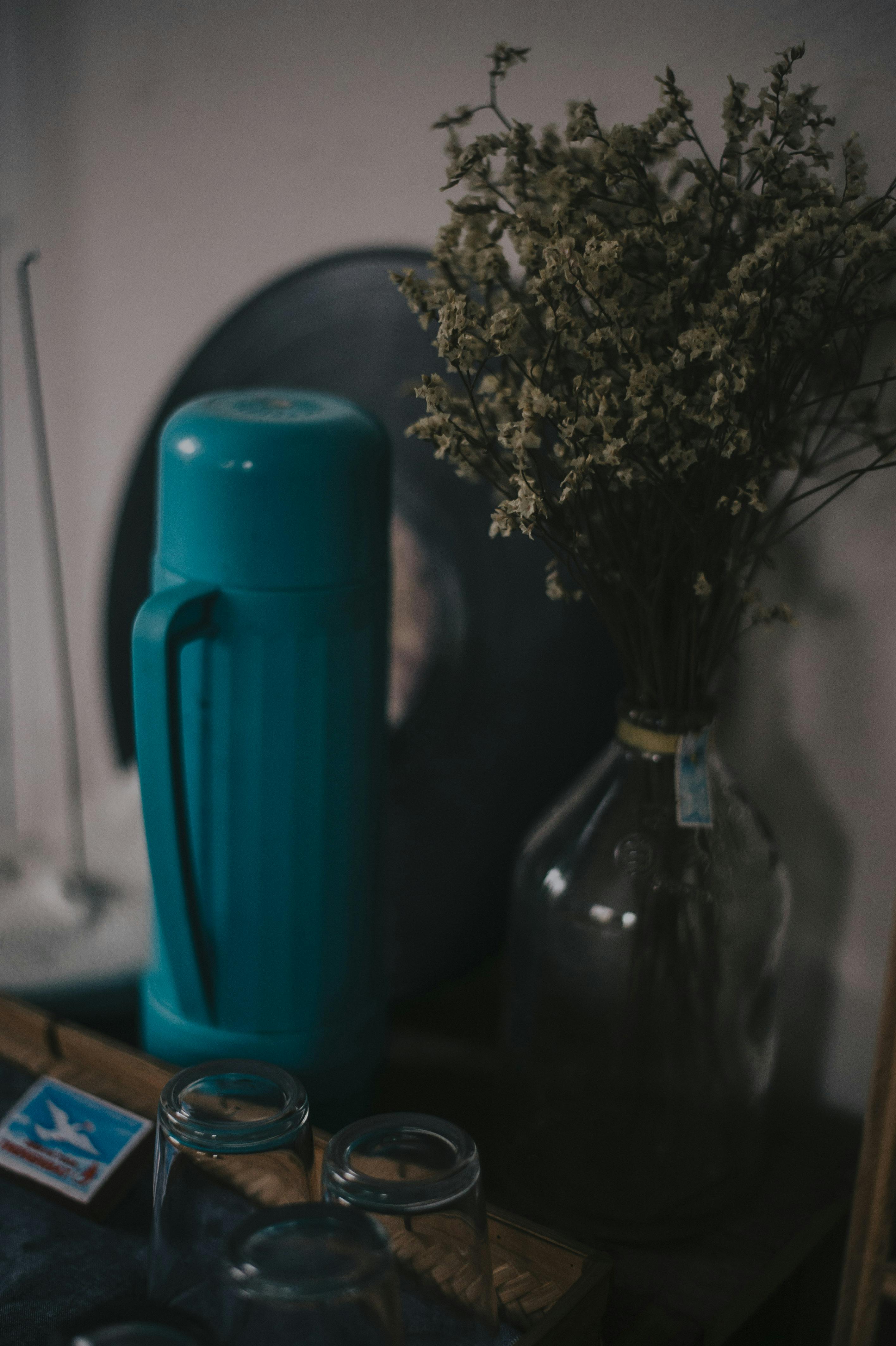 clear glass bottle with flowers near thermos