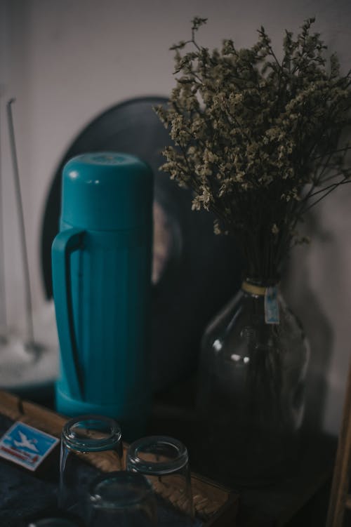 Clear Glass Bottle With Flowers Near Thermos