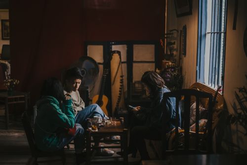 Free Three adults chat over coffee indoors with a guitar in the background. Stock Photo