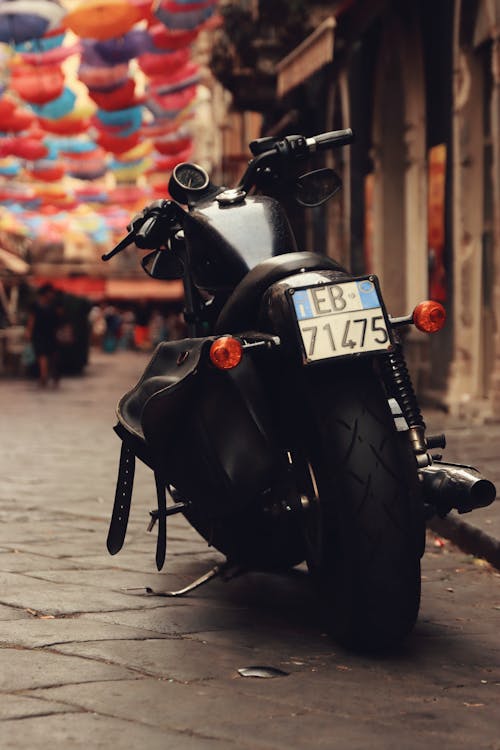 A Black Motorcycle Parked on a Street under Colorful Umbrellas 