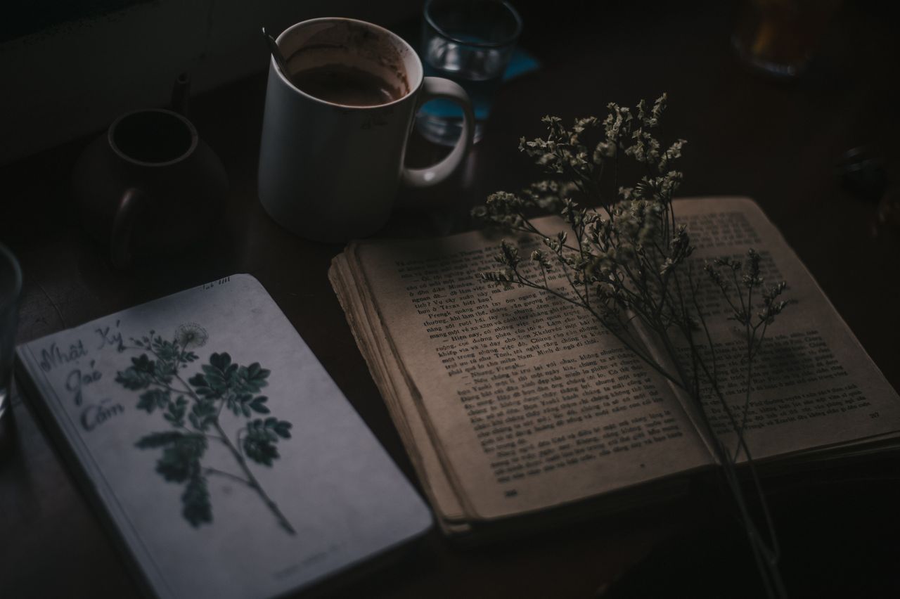 moody still life of vintage book coffee mug and dried flowers on a dar
