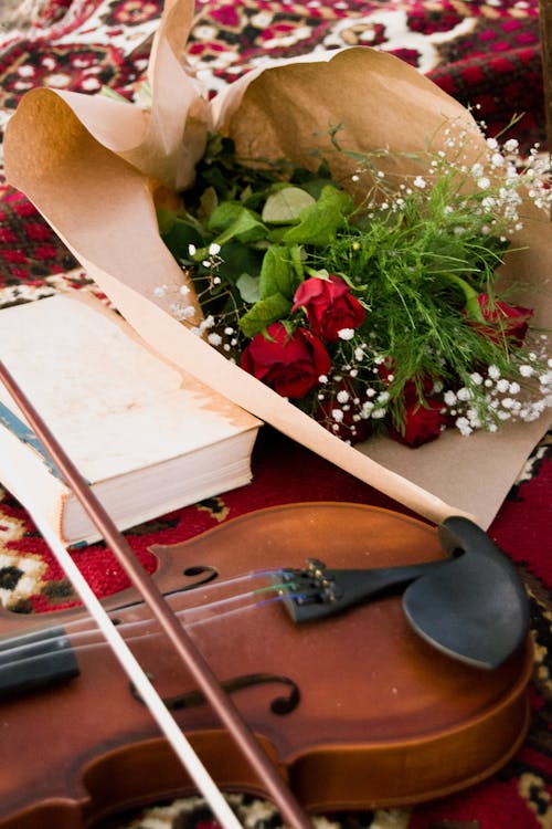 Bouquet of Roses Wrapped in Kraft Paper Lying Next to a Violin and a Book on the Carpet