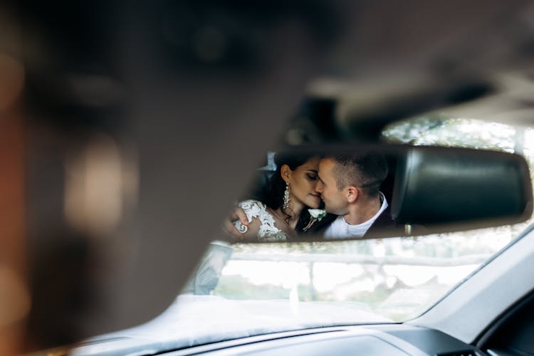 Rearview Mirror Reflection Of A Groom And Bride Kissing In A Car