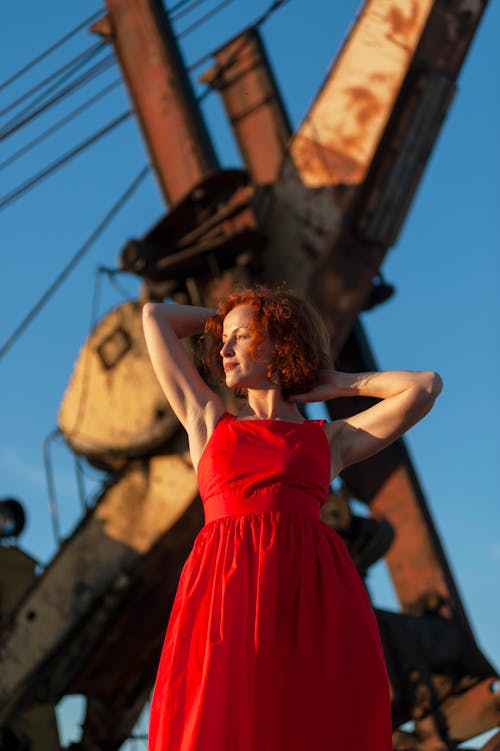 Redhead Model in Red Dress Posing against Rusty Industrial Equipment