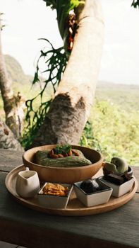 Wooden platter with green wrap and snacks, set against tropical scenery.