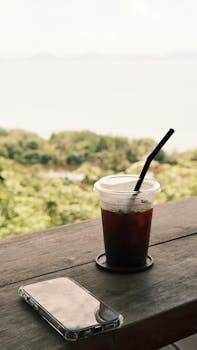 Refreshing iced coffee and smartphone on table with scenic outdoor view, perfect for relaxation themes.
