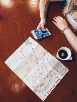 Top view of a woman using a smartphone with a map and coffee on the table, perfect for travel planning concepts.