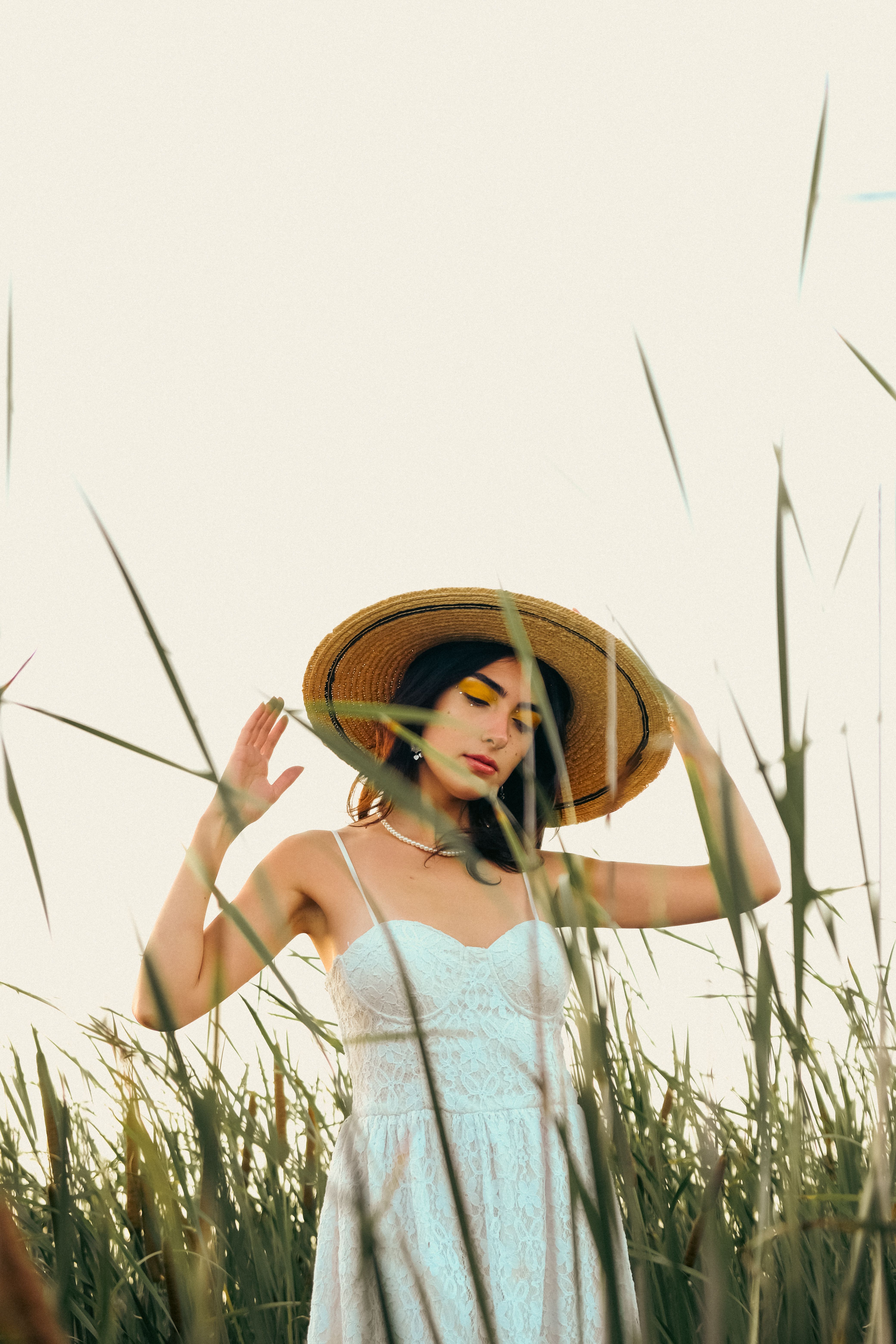Portrait of a woman in a white dress and sun hat standing in a field of tall grass.